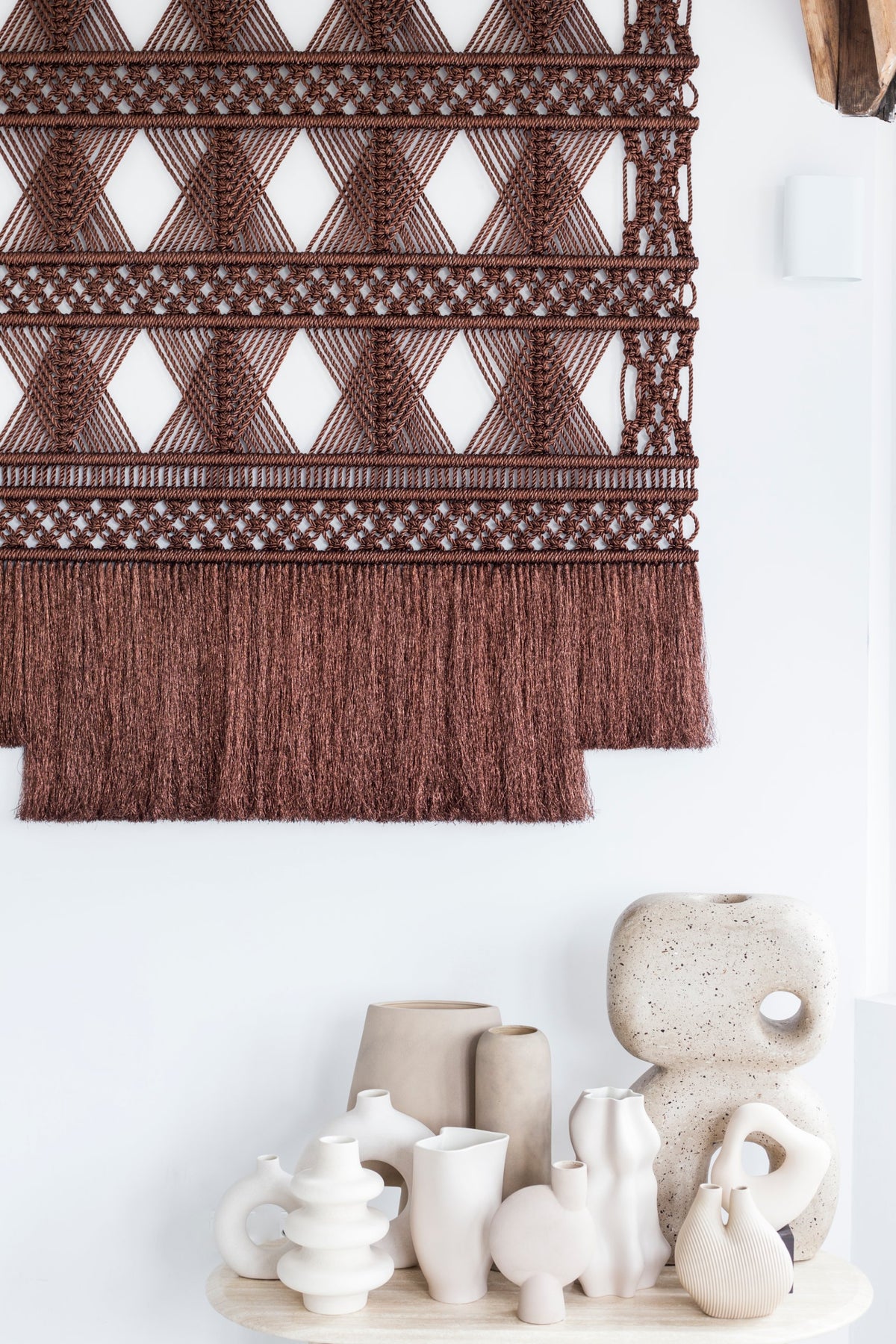 Detail of the brown metallic wall hanging above a shelf of white ceramic vases