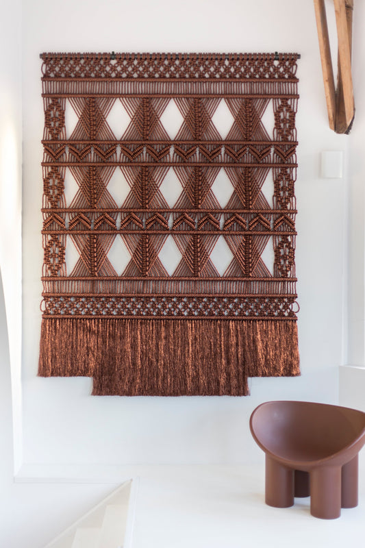 Brown metallic macramé wall hanging by Milla Novo, 180 × 250 cm, in a white interior with a brown chair